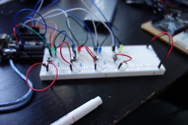 Circuit board with resistors, push buttons and LEDs sitting on a black desk